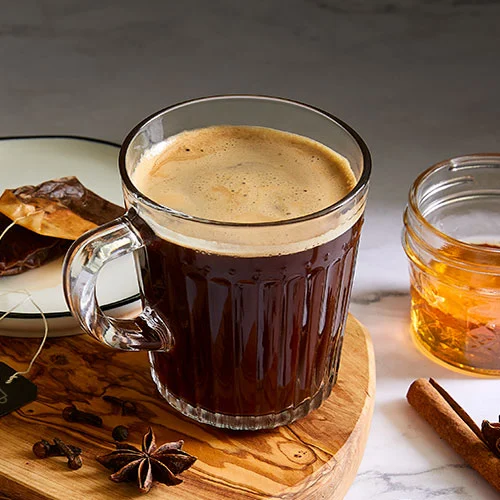 A steaming cup of Gluten-Free Dirty Chai, topped with a sprinkle of cinnamon, set against a cozy kitchen backdrop. Perfect for a homemade, budget-friendly treat.