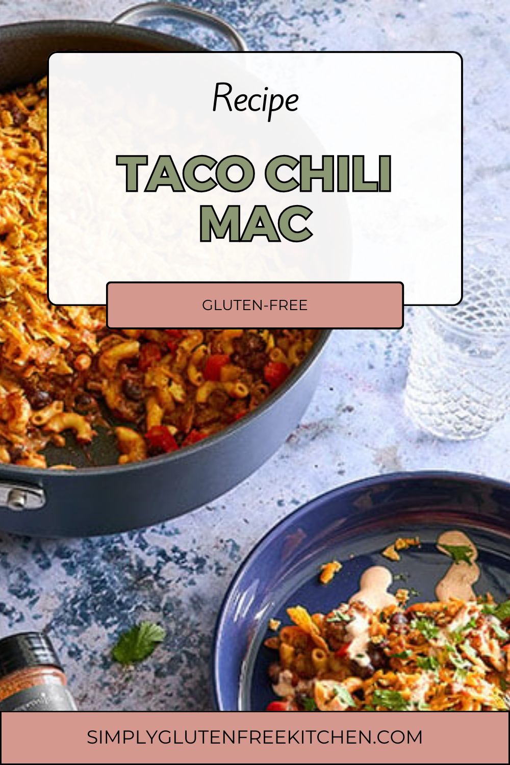 A skillet filled with colorful Gluten-Free Taco Chili Mac, featuring macaroni, ground beef, red bell peppers, black beans, and topped with melted cheddar cheese. A portion is served on a blue plate, garnished with fresh cilantro and a drizzle of sour cream sauce.