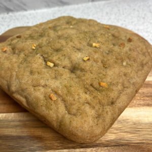 A thick, golden gluten-free focaccia bread infused with rosemary and roasted garlic, resting on a wooden board.