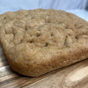 A close-up of a golden, fluffy gluten-free sourdough focaccia bread with a soft, airy texture.