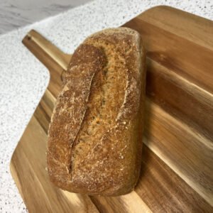 A fresh gluten-free sourdough sandwich loaf with a golden-brown crust, cooling on a wooden board.