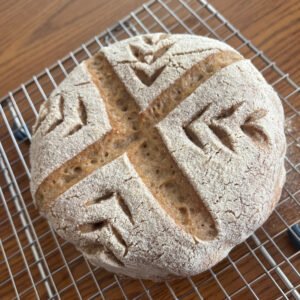 A round artisan-style gluten-free sourdough bread with a rustic, golden crust and a delicate flour dusting.