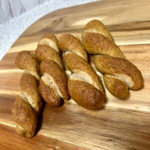 Freshly baked gluten-free sourdough twisted pretzel sticks with a crispy crust and soft center, arranged on a wooden board.