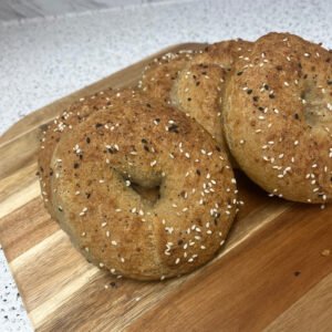 Freshly baked gluten-free bagels topped with an everything seasoning mix, arranged on a wooden board.